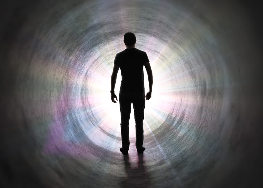 Life after death concept - Silhouette of man's soul is walking to bright light - rays of god inside tunnel